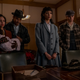 The ancestors of Archie, Tabitha, Fangs, and Toni, holding her baby, stand with downcast eyes in front of a mahogany desk.